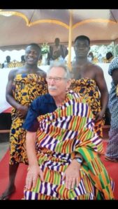 Prof. Spitznas sitzt in ein traditionelles Gewand der Akan Völker gekleiet, während hinter ihm links und rechts zwei Mitglieder der Akan Völker, ebenfalls in Gewandung, stehen.