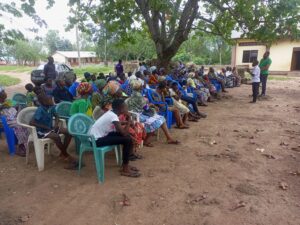 Eine große Menschenmenge sitzt auf Stühlen im Freien und wartet, aufgerufen zu werden.